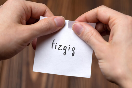 Hands of a man tearing a piece of paper with inscription fizgig