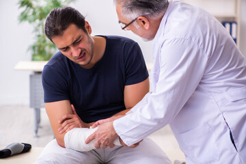 Obraz premium Young injured man visiting experienced male doctor traumatologis