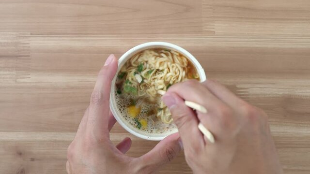 Stir the cup noodles with disposable chopsticks. Japanese instant ramen. Top view. High angle. Easy cooking. Living alone. Delicious food. Busy day