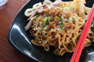 Mie Setan is an Indonesian food based on noodles and very spicy ingredients. devil noodles with sausage pieces, eggs, chips and flavoring vegetables. noodles on a wooden table