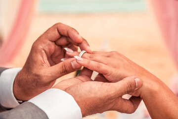 The groom puts a wedding ring on the bride’s finger.