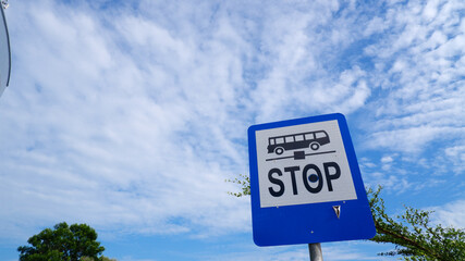 A blue bus stop sign and a beautiful blue sky with a white cloud
