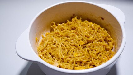 A tasty instant fried noodle (Indomie Goreng) mixed with scrambled boiled egg in a white bowl. Side view of delicious fried noodle