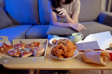Young asian woman takeaway eating full junk food on sofa and watch tv.