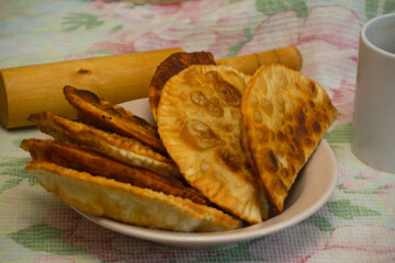 Russian kitchen. Deep-fried pasties stuffed with minced pork, onions and herbs on a plate on a tablecloth, side view, close-up, rolling pin on the background