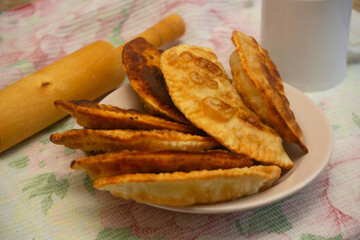 Russian kitchen. Deep-fried pasties stuffed with minced pork, onions and herbs on a plate on a tablecloth, side view, close-up, rolling pin on the background