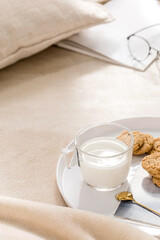 Plate with glass of milk, spoon and cookies on bed.