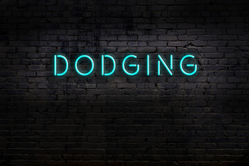 Neon sign. Word dodging against brick wall. Night view