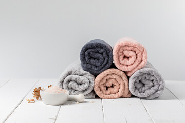 Stack of rolled cotton towels with a bowl of bath salts on gray background, copy space.