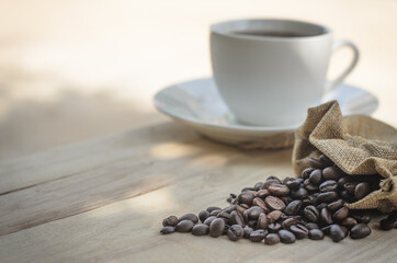 Hot coffee cup and coffee beans roasting on the wooden table in the morning