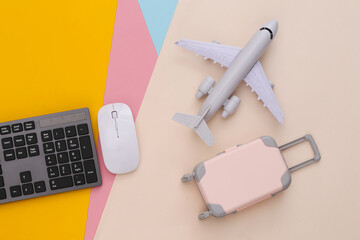 Travel flat lay. PC keyboard and mini travel luggage, air plane on colored background. Top view