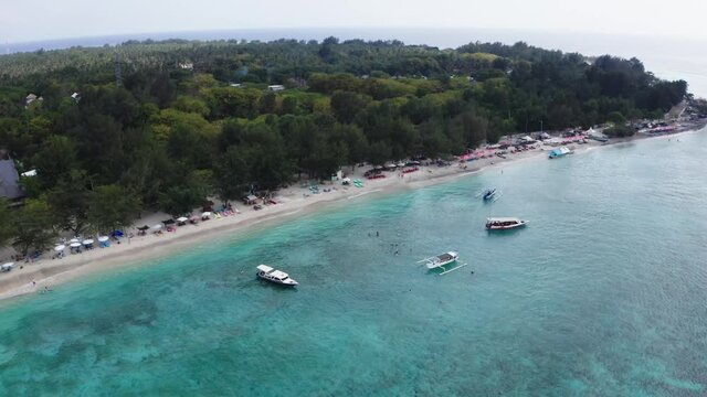 Aerial shot of the Gili Travangan Island. Crystal clear waters, green trees and cruise boats.