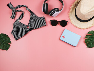 summer holiday concept, top view of  black and white stripe pattern  bikini swimsuit , passport and women's vacation accessories items  on pink background with tropical monstera leaves.