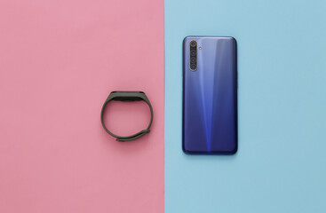 Modern smartphone and smart bracelet on a blue-pink pastel background. Top view