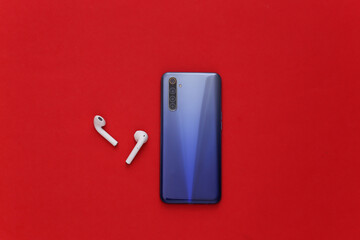 Modern gadgets. Modern smartphone with wireless earphones on red background. Top view. Flat lay