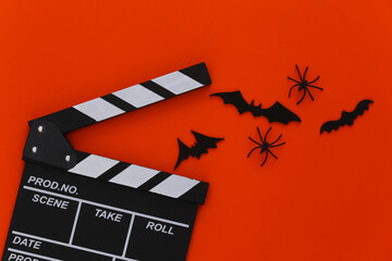 Horror movie, halloween theme. Movie clapperboard, spiders and flying decorative bats on orange background. Top view, flat lay