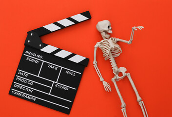 Horror movie, halloween theme. Movie clapperboard and decorative skeleton on orange background. Top...