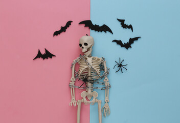 Skeleton wrapped in metal chain on pink blue pastel background with bats and spiders. Halloween...