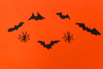 Halloween background, decorations and scary concept. Spiders and black bats fly over bright orange background. Top view