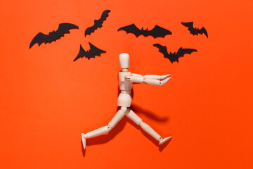 Halloween scary concept. Wooden puppet runs away on bright orange background with flying bats