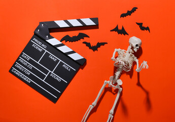 Horror movie, halloween theme. Movie clapperboard, skeleton and flying decorative bats on orange...