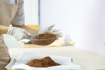 Closeup of woman, female baker hands while using flour sifter to make cocoa to bake homemade cake or bakery first time, learning new skills when home quarantine, COVID-19 or Coronavirus disease spread