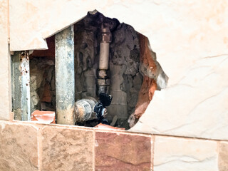 view of old water pipes and closed ball valve through broken ceramic tiles during repair of a heated towel rail