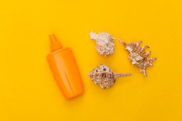 Sunblock bottle and seashell on a yellow background. Skin protection. Beach vacation. Top view