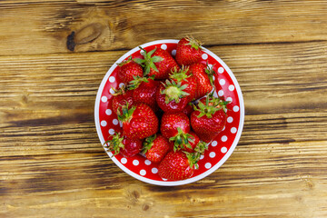 Fresh strawberry in a plate on a wooden table. Top view