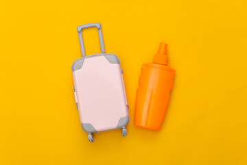 Beach vacation, travel concept. Mini toy travel luggage and sunblock bottle on yellow background. Top view. Flat lay