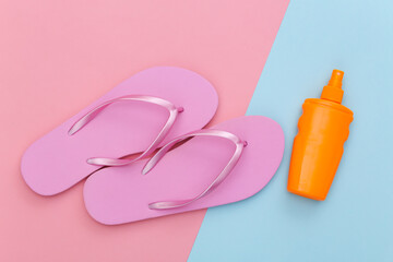 Beach vacation. Summer background. Sunblock bottle and flip flops on pink blue pastel background. Top view. Flat lay