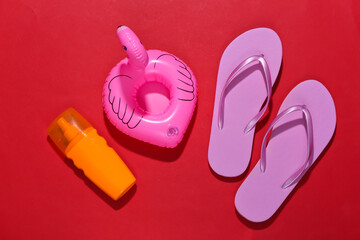 Beach vacation. Inflatable flamingo and sunblock, flip flops on bright red background. Top view