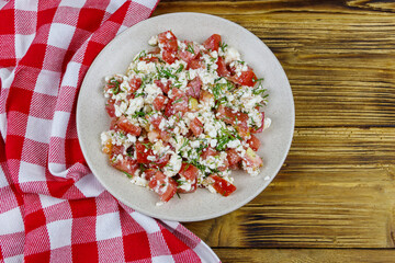 Tasty salad of tomato, cottage cheese, dill and olive oil on wooden table. Top view