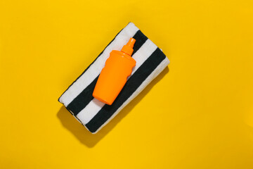 Beach vacation. Towel and sunblock bottle on bright yellow background. Top view. Minimalism