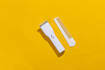 Wireless hair clipper and comb on yellow bright background. Top view