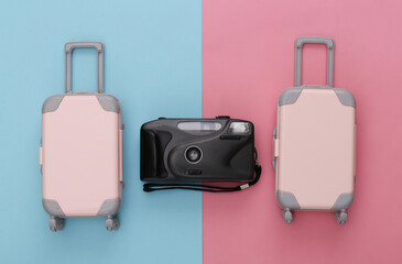 Two toy travel luggage and camera on pink blue pastel background. Travel planning. Top view. Flat lay