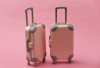 Two mini travel luggage suitcase on pink background. Travel still life, vacation or tourism concept.