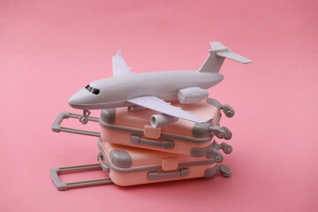 Two mini travel luggage suitcase and air plane on pink background. Travel still life, vacation or tourism concept.