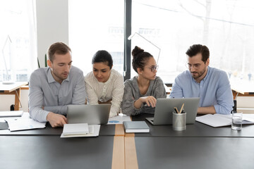 Concentrated multiracial colleagues sit at desk in office work in groups discuss project using...