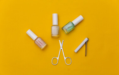 Manicure scissors, nail polish bottle and clippers on yellow background. Beauty concept. Nail care. Top view