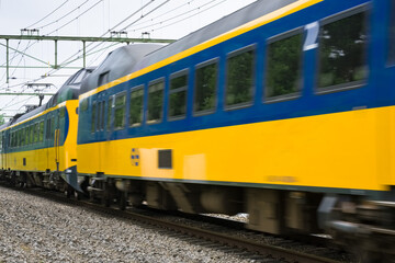 Fototapeta premium Dutch double-deck regional train with distinctive yellow and blue color and large windows passing by on a railway in Heerenveen in the Netherlands