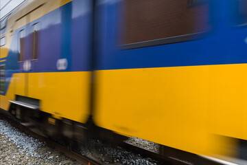 Dutch double-deck regional train with distinctive yellow and blue color and large windows passing by on a railway in Heerenveen in the Netherlands