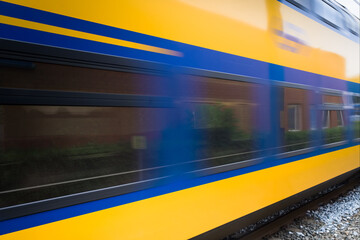 Dutch double-deck regional train with distinctive yellow and blue color and large windows passing...