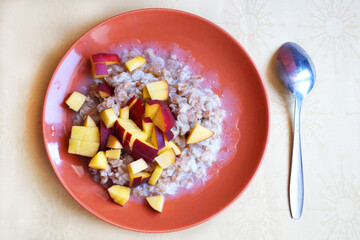 oatmeal porridge with chopped fresh peach in a plate with a spoon, vegetarian eating top view.
