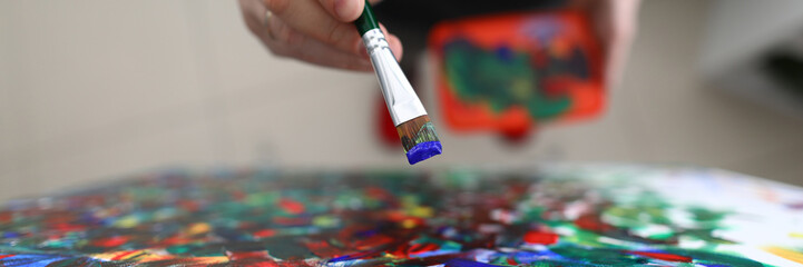 To view of persons hand applying oil paint on picture. Colourful brush strokes on canvas. Creative process of creating artwork. Hobby and modern art concept