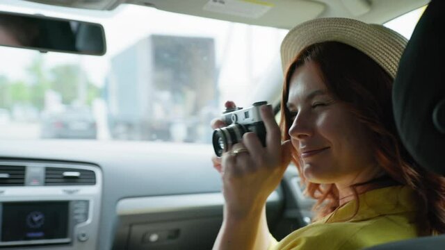 happy trip, smiling young woman photographer in straw hat uses retro camera while sitting in cars and takes pictures of his family while traveling