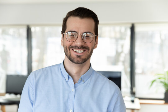 Headshot portrait of smiling confident young Caucasian businessman in glasses posing in office, happy excited male employee worker in spectacles show optimism success in work, employment concept