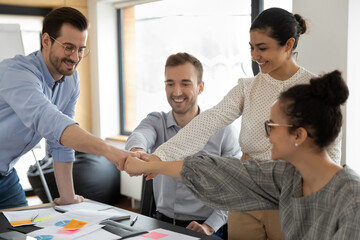 Overjoyed diverse employees join hands give fists bump motivated for shared group business result, happy multiracial colleagues engaged in teambuilding activity at meeting in office, teamwork concept