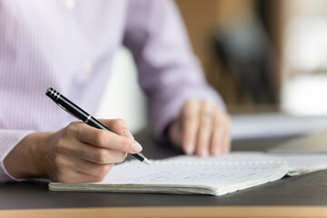Close up crop view of woman handwrite in notebook study online at home, smart concentrated female write in exercise book, summarize important data, prepare for exam session, take educational course