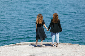 girls on vacation, hold each other's hands and admire the blue sea